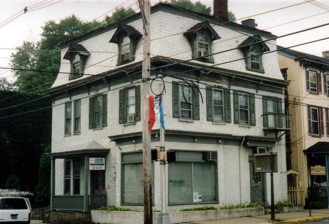 Painted mansard-roof building with green shutters and dormers on a town main street